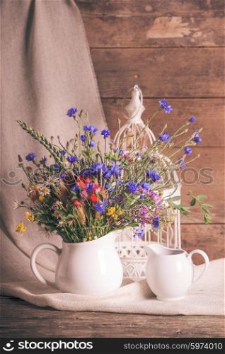 Wildflowers in white ceramic jug and cups on tray. Wildflowers in jug