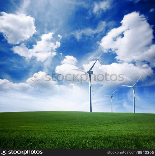 Wind power turbine station on green grass lawn over blue sunny sky