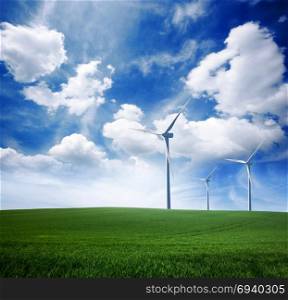 Wind power turbine station on green grass lawn over blue sunny sky