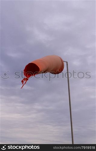 Wind sock (or conical textile tube) red and worn at one end against a grey sky.