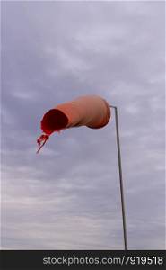 Wind sock (or conical textile tube) red and worn at one end against a grey sky.