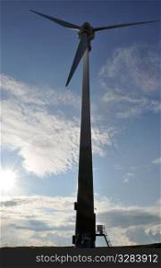 Wind turbine as alternative energy source against blue cloudy sky and bright sun