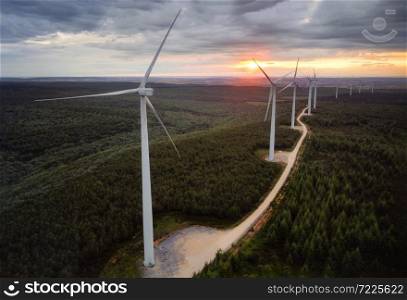 Wind turbine farm on beautiful forest landscape at sunset. Renewable energy production for green ecological world. Aerial view of wind mills farm park on evening mountain . . Wind turbine farm on beautiful forest landscape at sunset. Renewable energy production for green ecological world. Aerial view of wind mills farm park on evening mountain.
