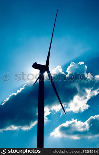 Wind turbine in the back light of the sun with blue sky and clouds.