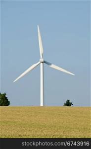 Wind turbine, wind mill. wind turbine seen from behind against blue sky and wheat field in the foreground
