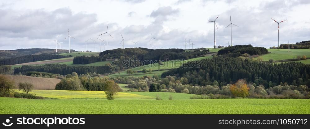 wind turbines and mustard seed field in rural landscape of south eifel in germany under cloudy autumn sky