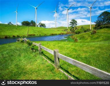 Wind turbines farm on a green grass rolling hills against blue sky and white clouds in summer. Concept of renewable clean energy and sustainability development business from wind energy.