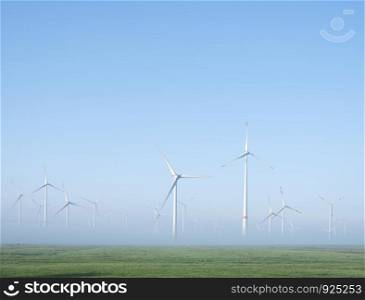 wind turbines in green meadow near aurich in german lower saxony on misty morning in august