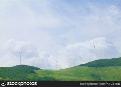 Wind turbines on lush, green, landscape with clouds.