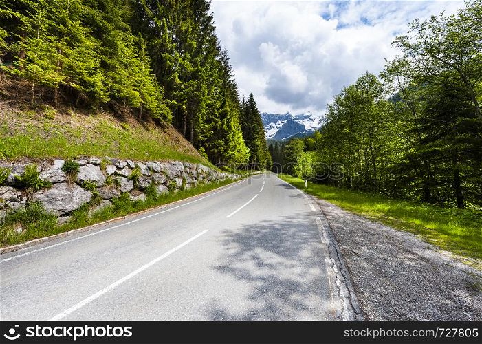 Winding asphalt road in Austrian landscape with forests, fields, pastures and meadows