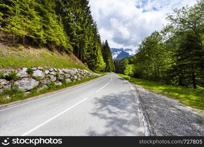 Winding asphalt road in Austrian landscape with forests, fields, pastures and meadows