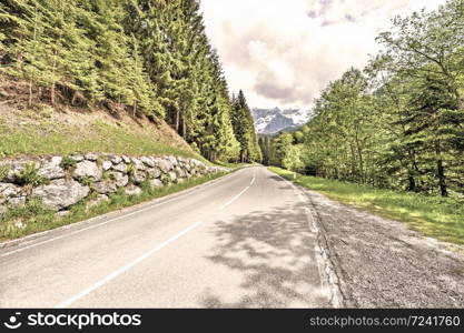 Winding asphalt road in Austrian landscape with forests, fields, pastures and meadows. Vintage style