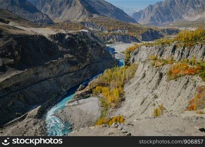 Winding turquoise blue water river flowing through Hunza Nagar valley along the Karakoram highway in autumn season with a view of Karakoram mountain range. Gilgit Baltistan, Pakistan.