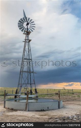 windmill with a pump and cattle water tank in shortgrass prairie against stormy sky, iPawnee National Grassland in Colorado near Grover