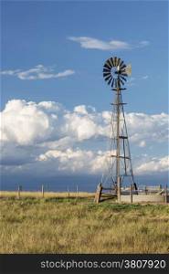 windmill with a pump and cattle water tank in shortgrass prairie against stormy sky, Pawnee National Grassland in Colorado near Grover