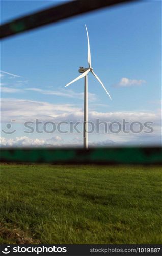 windmill with fresh green grass and clear blue sky in summer, energy concept near a fence. windmill with fresh green grass and clear blue sky in summer, energy concept near fence