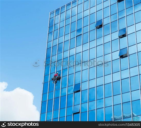 Window cleaner working on a glass facade suspended. Heavy work concept