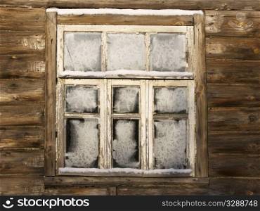 Window of abandoned country log house in russian village on winter sunny day