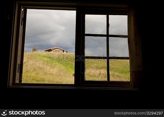 Window open to pasture with top of a dwelling visible over a hill