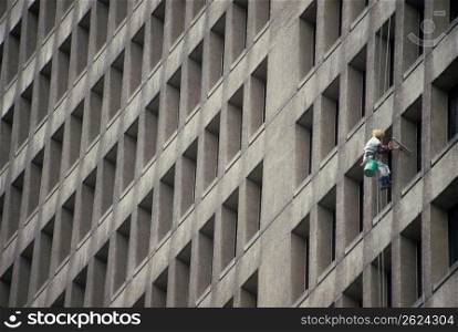 Window washer dangling precariously on side of tall office building washing windows