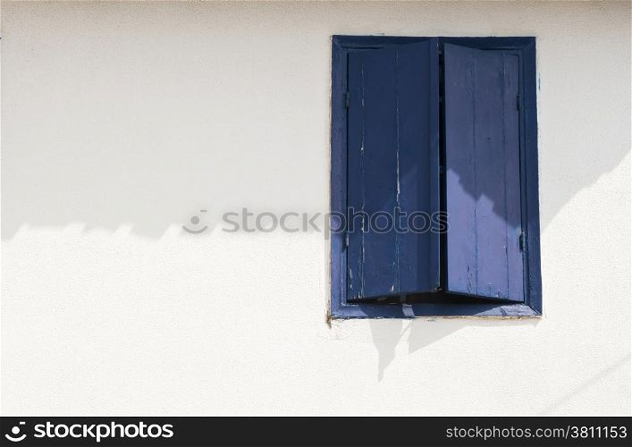 Window with blue wooden shutters on white house wall