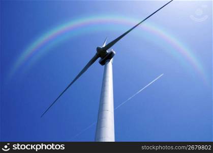 Windpower high up in a blue sky under a rainbow