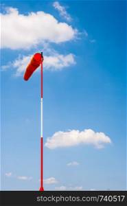 Windsock on pole in breeze against blue sky and cumulus clouds.