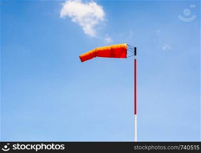 Windsock on pole pointing left in breeze against blue sky.