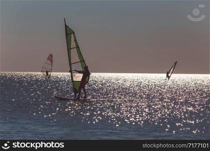 Windsurfers in the sea during sunset, active lifestyle.. Windsurfers in the sea during sunset, active lifestyle