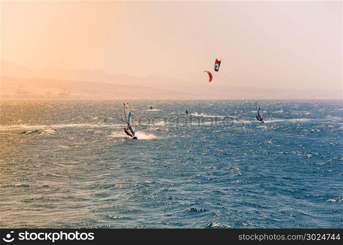 Windsurfers sailing in the Red Sea.Near the beach of Eilat, Israel.Bright orange light coming from the sun on the left.