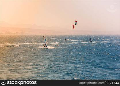 Windsurfers sailing in the Red Sea.Near the beach of Eilat, Israel.Bright orange light coming from the sun on the left.