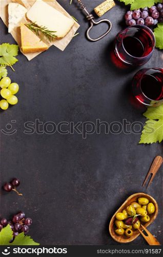 Wine and snack set. Variety of cheese, mediterranean olives, black and green grapes and glasses of red wine over dark background, top view, copy space