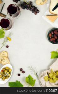 Wine and snack set. Variety of cheese, olives, prosciutto meat, baguette slices, black grapes and glasses of red wine over grey marble background, top view, copy space