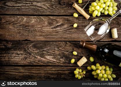 wine background of open wine bottle, wine glass and branches of white grapes on a dark wooden rustic background with blank space for a text