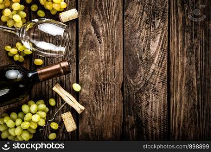 wine background of open wine bottle, wine glass and branches of white grapes on a dark wooden rustic background with blank space for a text