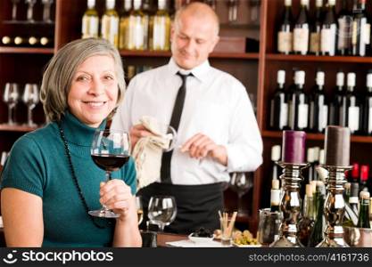Wine bar senior woman enjoy wine glass in front of bartender
