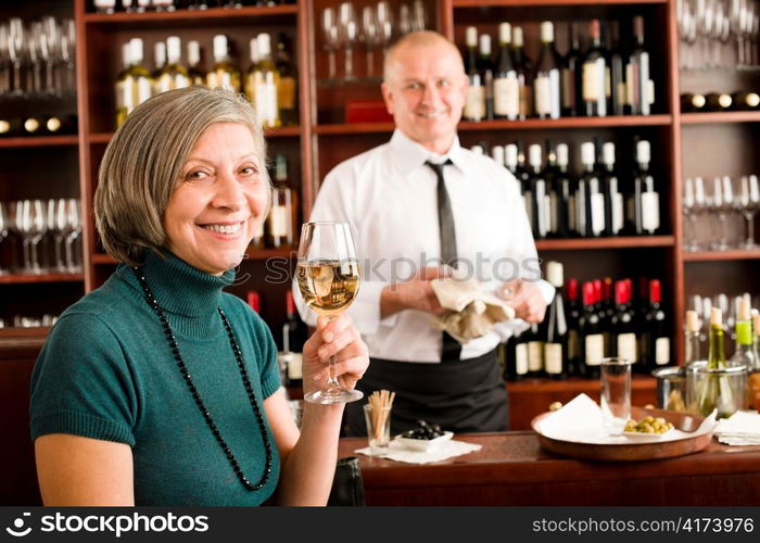 Wine bar senior woman enjoy wine glass in front of bartender