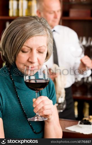 Wine bar senior woman smell wine glass in front of bartender