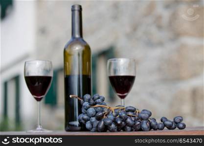 wine bottle and grapes on wooden table outdoor, focus on the grapes. Red wine