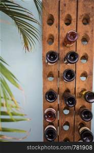 wine bottles in retro wooden rack with green house plant and blue wall, modern wine rack close-up. wine bottles in retro wooden rack with green house plant and blue wall, modern wine rack