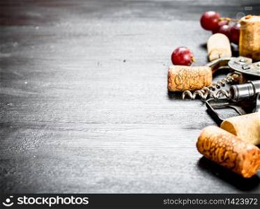 Wine corks with corkscrew and grape branch. On a black wooden background.. Wine corks with corkscrew and grape branch.
