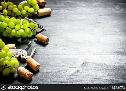 Wine corks with corkscrew and grape branch. On a black wooden background.. Wine corks with corkscrew and grape branch.