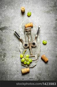 Wine corkscrew with grapes and corks. On the stone table.. Wine corkscrew with grapes and corks.