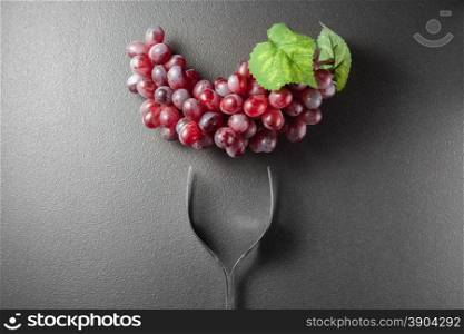 Wine glass made of forks and grape on black background