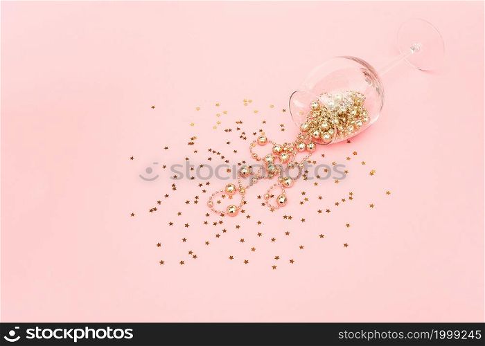 Wine glass poured out golden christmas decoration garland baubles and confetti stars on pink background. New Year, Christmas, Holiday concept Minimal style Top view Flat lay Copy space.. Wine glass poured out golden christmas decoration garland baubles and confetti stars on pink background. New Year, Christmas, Holiday concept Minimal style Top view Flat lay Copy space