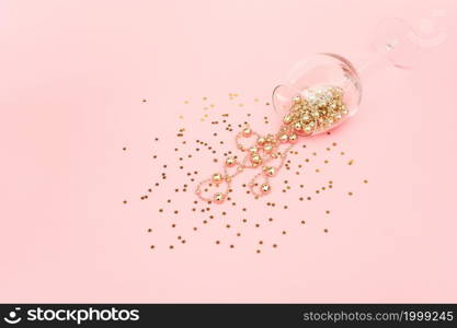 Wine glass poured out golden christmas decoration garland baubles and confetti stars on pink background. New Year, Christmas, Holiday concept Minimal style Top view Flat lay Copy space.. Wine glass poured out golden christmas decoration garland baubles and confetti stars on pink background. New Year, Christmas, Holiday concept Minimal style Top view Flat lay Copy space