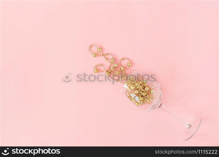 Wine glass poured out golden christmas decoration garland baubles on pink background. New Year, Christmas, Holiday concept Minimal style Top view Flat lay Copy space Greeting card, invitation.. Wine glass poured out golden christmas decoration garland baubles on pink background. New Year, Christmas, Holiday concept Minimal style Top view Flat lay Copy space Greeting card, invitation