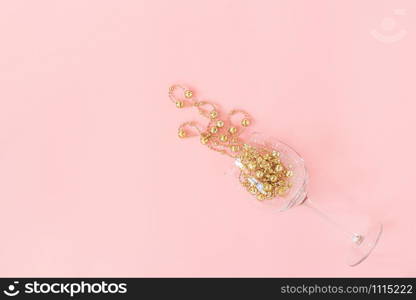 Wine glass poured out golden christmas decoration garland baubles on pink background. New Year, Christmas, Holiday concept Minimal style Top view Flat lay Copy space Greeting card, invitation.. Wine glass poured out golden christmas decoration garland baubles on pink background. New Year, Christmas, Holiday concept Minimal style Top view Flat lay Copy space Greeting card, invitation