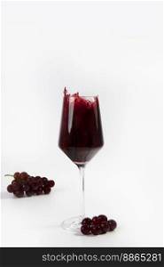 Wine glass with a splash of red wine and grapes isolated on white background copy space luxury. Wine Glass with a splash of red wine and grapes isolated on white background copy space