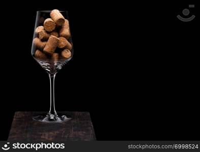Wine glass with corks inside on wooden board on black background.